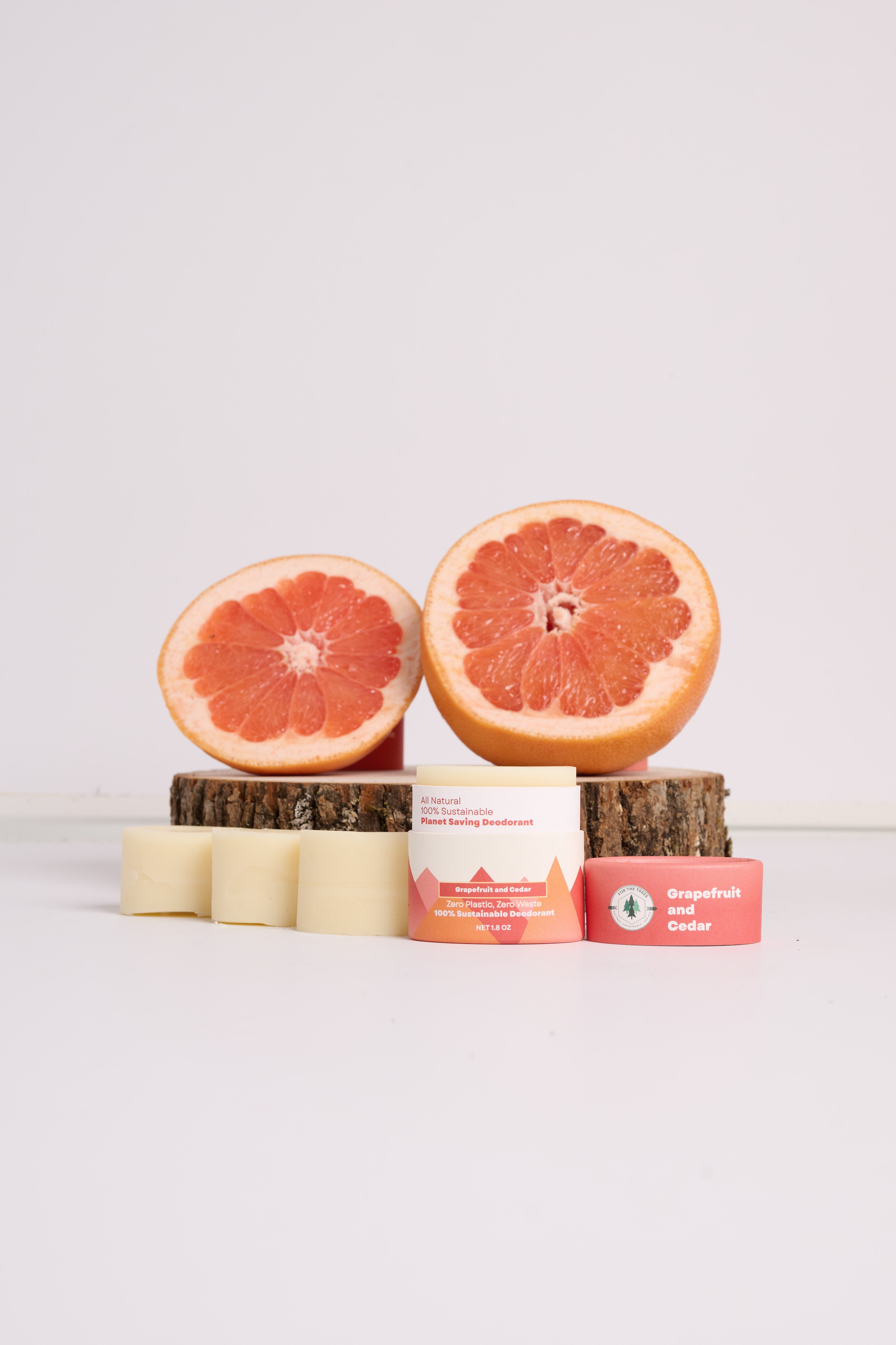A Travel Size Grapefruit and Cedar All Natural Deodorant (shown with refills, sitting in front of a grapefruit on a cedar wood block)