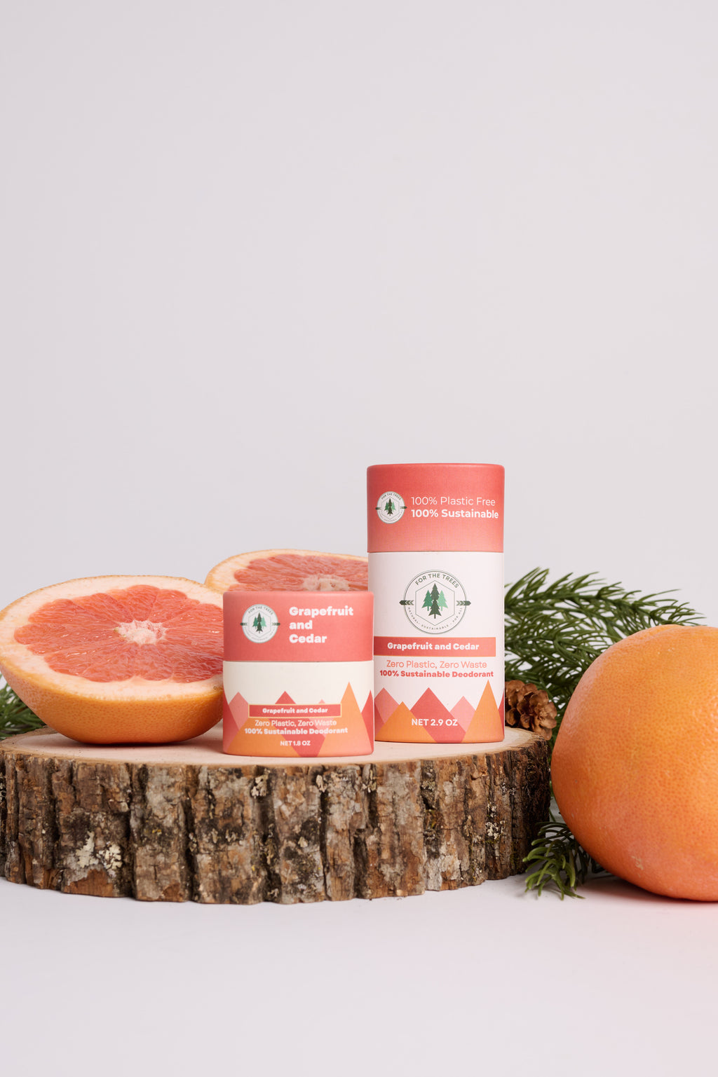 Two containers of For The Trees Brand 'Grapefruit & Cedar' All Natural Deodorant on a cedar log with Grapefruit and pine on a light gray background.